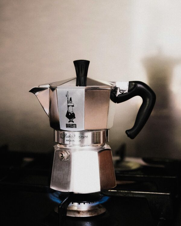 Classic Bialetti moka pot brewing coffee on a gas stove in a cozy kitchen.