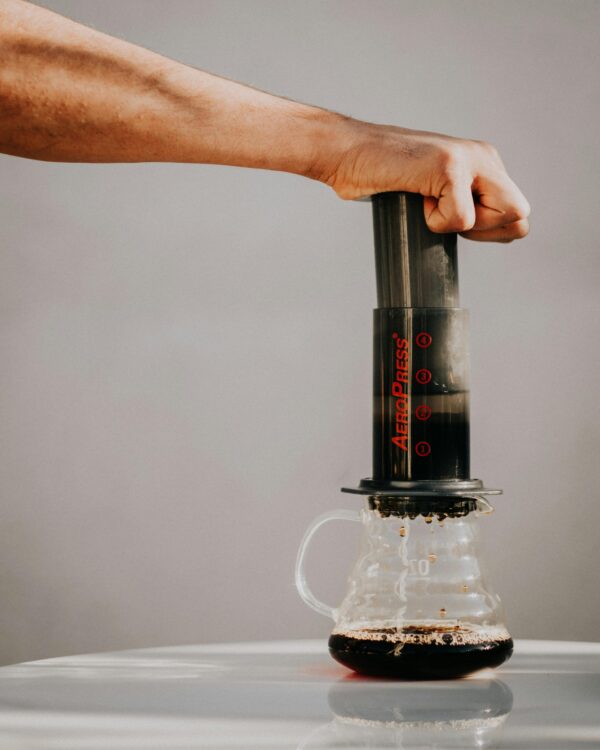A hand press brewing coffee using an Aeropress on a clear glass pitcher in a minimalist setting.
