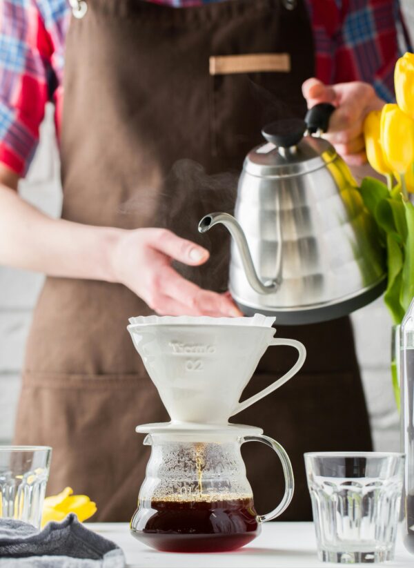 Barista preparing pour-over coffee using a dripper and stainless steel kettle.